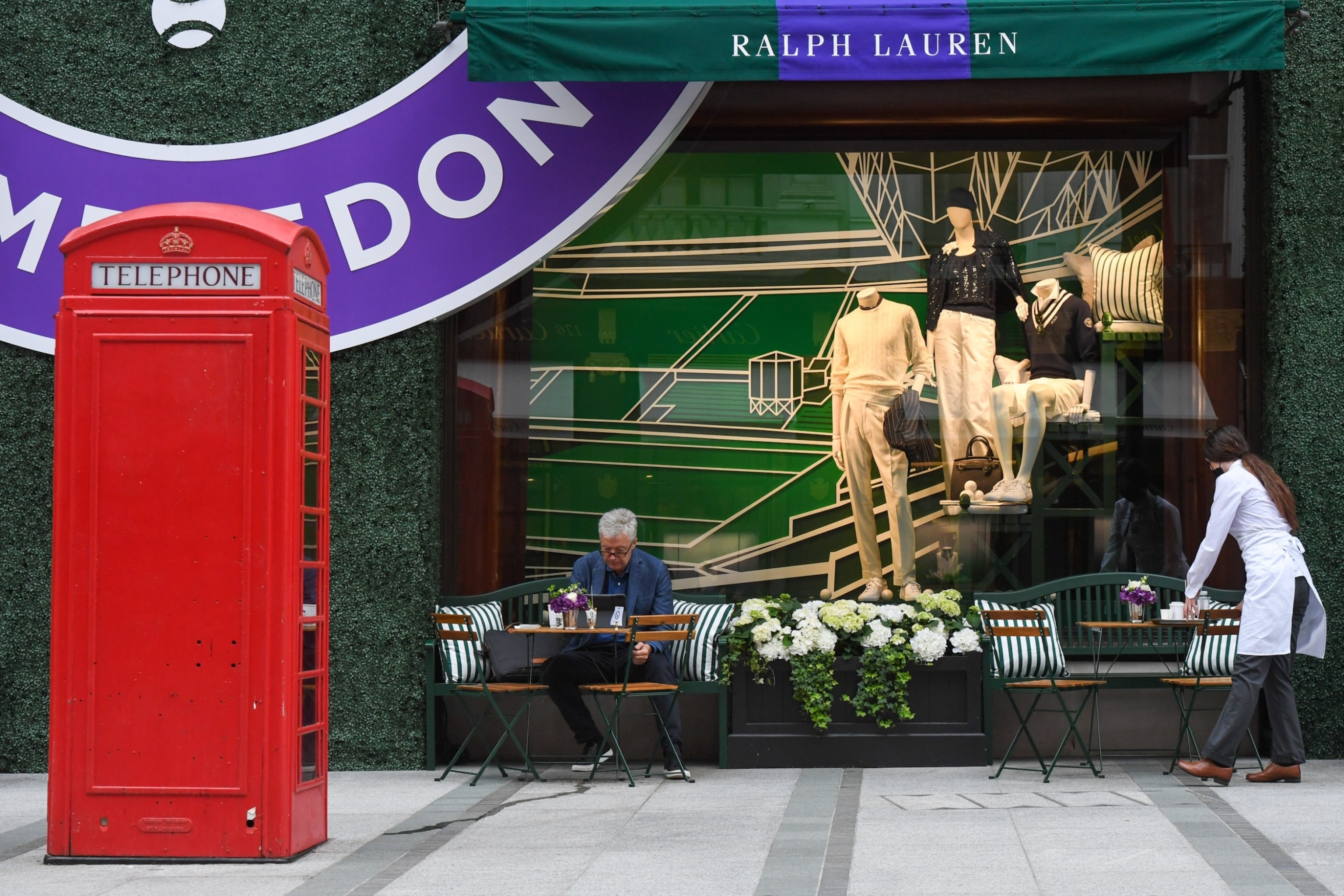 PHOTO: A waitress clears a table outside the Ralph Lauren Corp. store decorated to promote the Wimbledon Tennis Championships, in London, U.K., June 30, 2021.